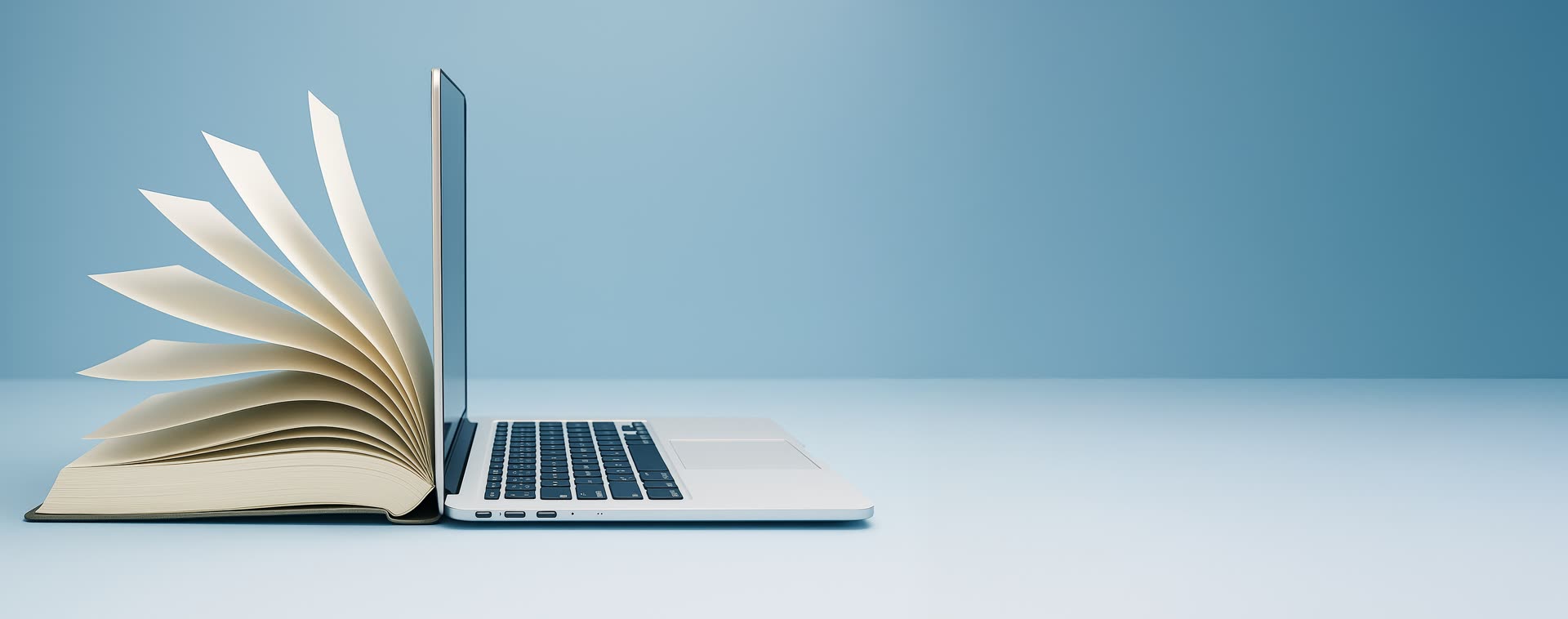 Libro abierto junto a un laptop, representando el aprendizaje y la capacitación